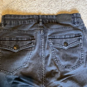 Svarta bootcut jeans från 157 - Svarta jeans från 157. Byxorna har snygga bakfickor med lock och knapp. 