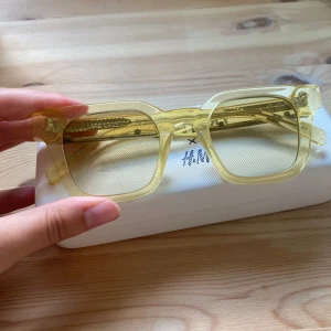 Gula transparenta glasögon CHIMI x H&M - Snygga fyrkantiga glasögon från CHIMI x H&M i transparent gul plast. De har en chunky båge och kommer med originalfodral och putsduk. Perfekt accessoar för att lyfta din stil med en pop av färg. Lite rostig på kanten som man kan se på sista bilden, inget som påverkar helhetsbilden