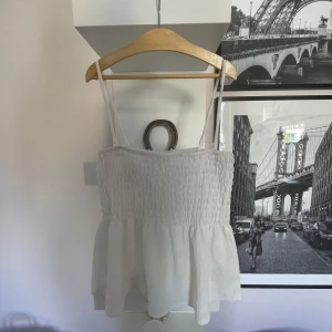 Söt top 😽💓 - Supersöt vit linnetopp från Gina Tricot i storlek XS. Toppen har smala axelband, smockad överdel och volangig nederdel som ger en luftig känsla. Perfekt för varma dagar och enkel att styla med jeans eller kjol.