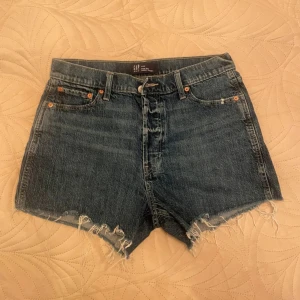 Högmidjade jeansshorts från GAP - Snygga blå denimshorts från GAP med hög midja och råa, fransiga benslut. Klassisk femficksmodell och knappgylf. Perfekta för sommaren och ger en avslappnad vibe till din outfit.