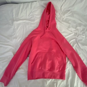 Rosa hoodie med huva och magficka - Säljer en snygg rosa hoodie med huva och dragsko. Tröjan har en klassisk känguruficka framtill och långa ärmar. Perfekt för dig som gillar en enkel men färgstark stil. Passar till chill dagar eller när du vill sticka ut lite extra.