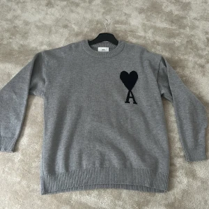 Grå stickad tröja från Ami Paris - SkitSnygg grå stickad tröja från Ami Paris med svart hjärta. Tröjan är i nyskick och använd max 2gånger. Den har normal passform och passar från allt runt 175-183 beroende på hur du vill att den ska sitta. 