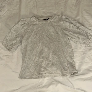 Ljusgrå t-shirt med puffärm från LMTD - Snygg ljusgrå t-shirt från LMTD i mjuk bomull. Modellen har korta puffärmar och rundad hals med ribbad kant. Perfekt för dig som gillar enkel stil med en twist. Passar dig som vill ha en chill och clean look. En liten sminkfläck längst ner på tröjan, men inget man tänker på🫶🏼