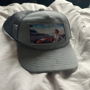 revenite keps limited edition - Snygg grå keps med mesh på baksidan och justerbar snapback. Framtill finns en stor patch med motiv av en sportbil, yacht och en kvinna. Perfekt för dig som gillar racing och streetstyle. Kepsen har böjd skärm och coolt tryck som sticker ut. man kan inte heller köpa den längre.