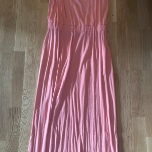 Lång rosa klänning med resårmidja - Säljer en lång, ljusrosa klänning med resår i midjan. Klänningen har en enkel och flowy design, perfekt för varma dagar. Den är ärmlös och har en mjuk, bekväm känsla. Passar dig som gillar en feminin och avslappnad stil.