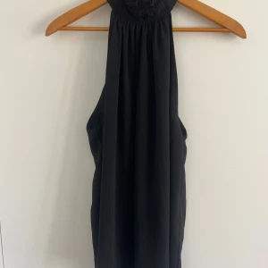 Svart haltertopp från H&M - Supersnygg svart topp från H&M med halterneck och rynkad krage. Toppen är ärmlös och har en luftig, flowy passform som ger en cool och avslappnad vibe. Perfekt för dig som gillar stilrena och enkla plagg med en twist.