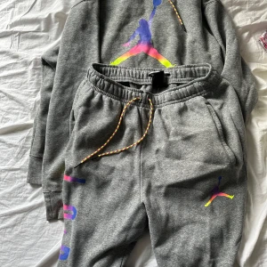 Grå Jordan mjukisbyxor med färgglada detaljer - Säljer ett par grå mjukisbyxor från Jordan med färgglada snören och tryck i neonfärger. Byxorna har elastisk midja, sidofickor och ett stort Jumpman-tryck i blått, rosa och gult på benet. Perfekt för chill eller sportiga dagar.