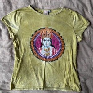 Grön t-shirt med tryck - Cool grön t-shirt från Indiska med ett tryck i mitten som har lila, orange och guldiga detaljer. T-shirten har rund hals och korta ärmar.