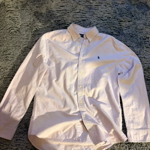 Ljusrosa skjorta från Ralph Lauren S - Klassisk ljusrosa skjorta från Ralph Lauren med button-down krage och broderad logga på bröstet. Skjortan har långa ärmar, knappar framtill och är tillverkad i mjuk bomull. Perfekt för en clean och stilren look.