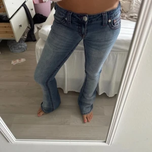 True Religion bootcut jeans blå - Säljer ett par blå bootcut jeans från True Religion med röda kontrastsömmar och klassiska detaljer. Jeansen har låg midja och fem fickor, tillverkade i jeansmaterial. Perfekta för dig som gillar en snygg och tidlös look.