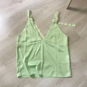 Ljusgrön linnetopp med knytband - Säljer en ljusgrön linnetopp med v-ringning och smala axelband som knyts på axlarna. Toppen har en luftig passform och är perfekt till sommaren. Materialet känns svalt och lätt, vilket gör den superbekväm att bära.
