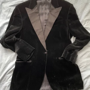 Svart sammetskavaj till smoking - Svart sammetskavaj med sidenslag. Används till smoking (black tie). Okej skick. Finns små fläckar här och där Mått- axlar: 46cm, ärmar: 62cm, byst: 55/110cm, längd 76cm
