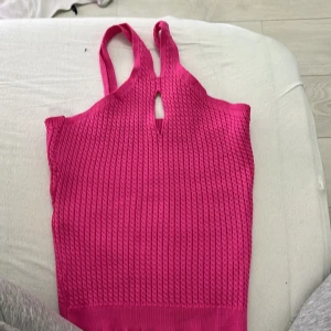 Stickad rosa linnetopp med nyckelhålsdetalj - Säljer en stickad rosa linnetopp med breda axelband och en snygg nyckelhålsdetalj framtill. Toppen har en ribbad struktur och är perfekt för varma dagar. Passar dig som gillar färg och vill sticka ut lite extra.