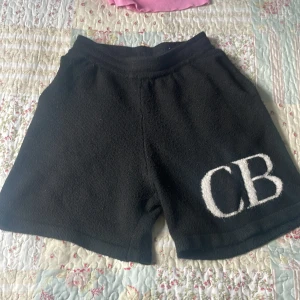Svarta shorts från Cole Buxton XL - Svarta shorts från Cole Buxton i storlek XL. Mjukt och lite fluffigt material med stora vita CB-bokstäver broderade på ena benet. Perfekta för chill dagar eller när du vill ha en clean och enkel look.