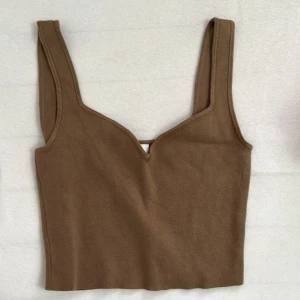 Beige stickad linnetopp - Snygg beige stickad linnetopp med breda axelband och en subtil v-ringning framtill. Perfekt för att styla med jeans eller kjol för en trendig look. Mjuk och skön mot huden, passar till både vardag och när du vill känna dig extra fin.