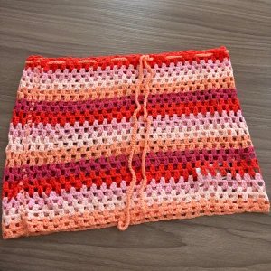 Virkad kortkjol i rosa och rött - Superfin virkad kortkjol med snörning i midjan. Aldrig använd och passar perfekt som en coverup över bikini💗