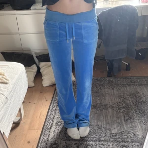Blå velour mjukisbyxor med snörning - Säljer ett par blå mjukisbyxor i mjuk velour med bred resår i midjan och snörning framtill. Byxorna har raka ben, stora fickor fram och en bakficka med knappar. Perfekta för chill dagar hemma eller när du vill vara extra comfy.