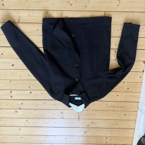 Svart overshirt från These glory days - Stilren svart overshirt från These glory days med raka linjer och stora bröstfickor. Jackan har knäppning framtill med fyra knappar och är tillverkad i en mix av ull, polyester och viskos. Perfekt för lager-på-lager och enkel att matcha med allt