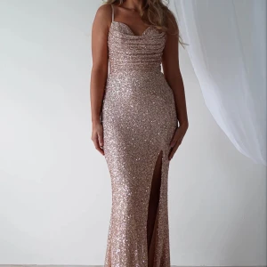 Balklänning guld - Snygg klänning i guld med tunna axelband som även går att justera, glittrigt paljettmaterial och draperad överdel. Klänningen har en figurnära passform och en hög slits framtill. Perfekt för bal eller festkvällar. Klänningen har även en ”inbyggd bh” så brösten ser bra ut i klänningen. Endast använd en gång på min bal och klänningen har inga skador förutom underkjolen på släpet som är smutsigt, då jag gick med den ute. Det är inget som syns vid användning då de andra täcker för. Org pris 1800.