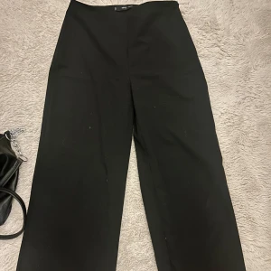 Svarta vida kostymbyxor från MNG - Säljer ett par svarta kostymbyxor från MNG i storlek 36. Byxorna har hög midja och ett snyggt wide fit-snitt som ger en clean och modern look. Perfekta att styla med crop top eller oversized skjorta. Materialet känns mjukt och följsamt.