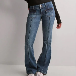 Blå bootcut jeans från Nelly - Snygga blå bootcut jeans från Nelly Jeansen har stora fickor framtill och dubbla knappar i midjan. Strl 36 i fint skick. Säljs ej längre på Nelly. Små bristningar längst ner på baksidan av benen som syns i de två sista bilderna