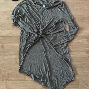 Beige långärmad klänning med knut - En beige långärmad klänning i mjukt material med snygg knutdetalj framtill. Modellen är rak och har en avslappnad passform, perfekt för dig som gillar en enkel men trendig look. Klänningen är enkel att styla och har en neutral färg som passar till mycket.