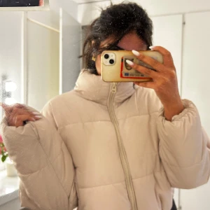 Beige pufferjacka med dragkedja  - Säljer en beige pufferjacka med hög krage och hel dragkedja framtill. Jackan är quiltad och har en loose passform med långa ärmar och elastisk nederkant. Perfekt för kyliga dagar och enkel att styla till olika outfits.
