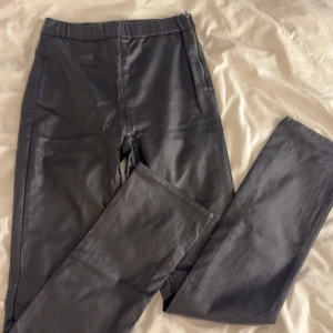 Svarta bootcut byxor med slits i skinnimitation - Säljer ett par svarta, högmidjade byxor i skinnimitation med bootcut passform och slits. Byxorna har dragkedja i sidan och bakfickor. 