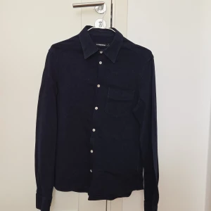 manchesterskjorta J.Lindeberg - Snygg mörkblå skjorta från J.Lindeberg i mjuk manchester. Klassisk krage, vita knappar och en bröstficka. Långärmad modell med stilren look, perfekt för dig som gillar en clean och tidlös stil. Liten i storleken.
