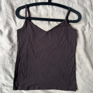 Mörkbrunt linne med smala axelband - Stilren mörkbrun linnetopp med smala axelband och v-ringning. Att go back to basics kan vara så skönt ibland. 