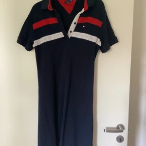 Tommy Hilfiger långklänning XL - Snygg långklänning från Tommy Hilfiger i marinblått med röda och vita detaljer. Klänningen har korta ärmar, krage och knappar framtill. Materialet är mjuk bomull som känns skönt mot huden. Perfekt för dig som gillar sportig och klassisk stil.  Storlek L/ XL går bra vilket som. Priset går att diskutera.