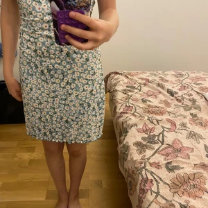 Blommig ljusgrön kort klänning - Supersöt kort klänning med grön botten och vita blommor över hela tyget. Axelbandslös modell med en liten rosett fram. Materialet känns lätt och skönt mot huden. Aldrig använd!!!!!Pris kan diskuteras 💗