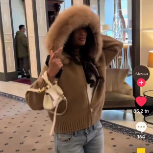 alessa jacket  - Supermjuk och trendig beige teddyjacka med stor fluffig pälshuva och dragkedja framtill. Jackan har ribbade muddar och midja för en snygg passform. Perfekt för kalla dagar när du vill vara både varm och stylish.