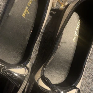 Svarta och vita ballerinaskor med rosett - Chunky ballerinaskor i svart och vitt från Vienna Shoes. Skorna har lackad finish, rund tå och en söt rosett framtill. De har en kraftig platt sula och dekorativt pärlband. Perfekta för dig som vill sticka ut med en klassisk men edgy look.