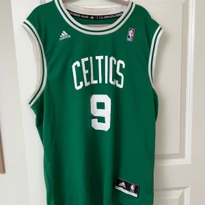 Boston Celtics Rondo #9 baskettröja Adidas - Grön baskettröja från Adidas med Celtics-tryck och nummer 9, inspirerad av Rajon Rondo. Ärmlös modell med vita detaljer och klassisk NBA-logga på bröstet. Tillverkad i lätt och ventilerande material, perfekt för sport eller streetwear. Nypris 899. Använd men omhändertagen. 