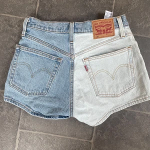 Levis jeansshorts  - Unika Levi's shorts med en cool, tvådelad design! Den ljusa och mörka denimtvätten ger en snygg kontrast. I fint skick. Storlekslappen är bortklippt men troligtvis w25. Klassisk Levi's kvalitet och passform.