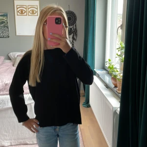 Svart långärmad tröja från Zara - Enkel svart långärmad tröja från Zara med rund hals och ribbade muddar. Tröjan har en liten slits bak i nederkanten som ger en snygg detalj. Perfekt till jeans eller kjol för en clean look.