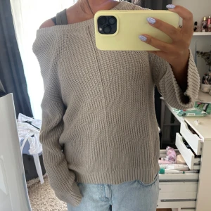 Beige offshoulder stickad tröja - Säljer en beige stickad tröja med offshoulder-modell och avslappnad passform. Tröjan har en markerad söm längs ryggen och bred ribbad kant vid ärmslut och nederkant. Perfekt för dig som gillar en chill och trendig look. Med dragkedja på ryggen!