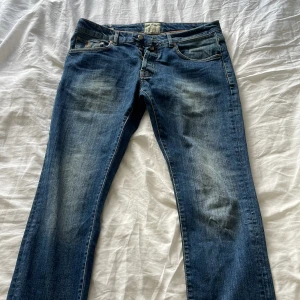 Blå jeans från Morris, storlek 34/34 - Snygga blå jeans från Morris i klassisk tvätt med lätt slitning på låren. Modellen har raka ben och fem fickor samt detaljerade bakfickor. Jeansen är tillverkade i bomull och har en normal passform. Perfekta för dig som gillar stilrena och tidlösa jeans.