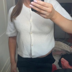 Vit stickad kortärmad topp från Pieces - Superfin vit stickad topp från Pieces med korta ärmar och rund hals. Modellen är croppad och har knappar framtill. Perfekt att styla med höga jeans eller kjol för en chill och trendig look.