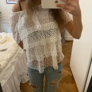 Vit spetsblus med volanger - Superfin vit blus i spets med flera lager volanger. Blusen är genombruten och har korta ärmar, perfekt för en somrig look. Sitter löst och passar perfekt till jeans eller kjol för en trendig outfit.