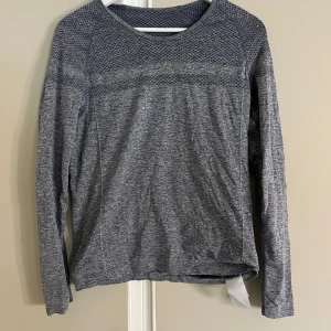 Grå långärmad tröja från Röhnisch - Superskön grå långärmad tröja från Röhnisch med diskret mönstrad struktur upptill. Perfekt för träning eller chill dagar. Materialet är mjukt och stretchigt, och passformen är normal. Snygg och enkel att matcha med det mesta.
