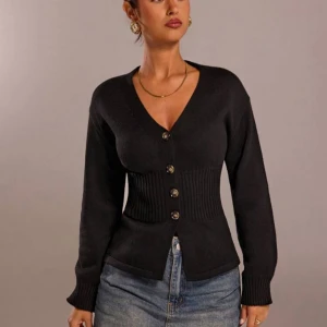 Svart ribbad kofta med v-ringning - Snygg svart kofta med v-ringad hals och markerad midja i ribbad stickning. Fyra knappar framtill och långa ärmar med ribbade muddar. Perfekt att styla med jeans för en chill och trendig look.