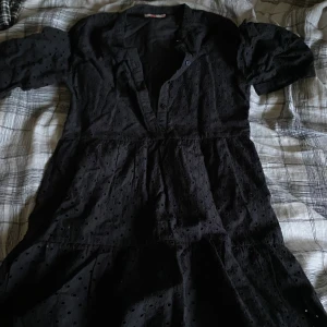 Svart kortklänning från WE med prickar - Säljer en svart kortklänning från WE med diskret prickigt mönster. Klänningen har trekvartsärm, v-ringad hals och knappar framtill. Materialet känns mjukt och lätt, perfekt för dig som gillar enkel men snygg stil.