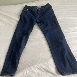 Blå jeans från Tiger of Sweden - Snygga mörkblå jeans från Tiger of Sweden med klassisk femficksdesign och kontrastsömmar. Modellen har rak passform och normal midja, tillverkade i slitstarkt bomullsjeansmaterial. Perfekta för dig som gillar stilrena och tidlösa jeans.