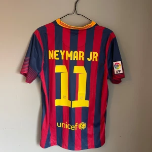 FC Barcelona Neymar Jr matchtröja - Säljer en vintage FC Barcelona Neymar Jr matchtröja med nummer 11. Tröjan är kortärmad, har rödblåa vertikala ränder, gul Nike-logga och klubbmärke på bröstet. Materialet är Dri-FIT polyester och har LFP-patch på ärmen. Snygg V-ringad krage i gult och rött. Säljer på grund av att den inte används