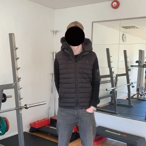 Svart väst från Moose Knuckles - Säljer en svart väst från Moose Knuckles. Jackan har en huva och dragkedja framtill. Perfekt för våren med sin stilrena design och bekväma passform.
