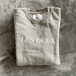 Grå sweatshirt från Les Deux - Säljer en stilren grå sweatshirt från Les Deux med tryck framtill. Tröjan har rund hals och långa ärmar, perfekt för en avslappnad look. Tillverkad i Turkiet. Priset kan diskuteras😄