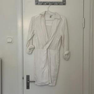 Vit omlottklänning från Nelly - Säljer en stilren vit omlottklänning från Nelly. Klänningen har långa ärmar. Stor i storleken