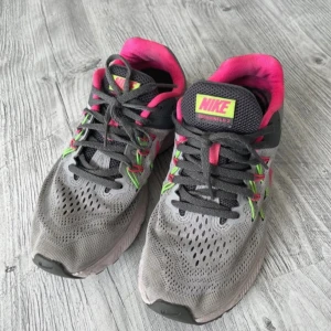 Grå och rosa Nike löparskor Zoom Winflo 2 - grå Nike Zoom Winflo 2 löparskor med rosa och gröna detaljer. Skorna har snörning en ventilerande ovandel och en slitstark sula. Storlek EU 38